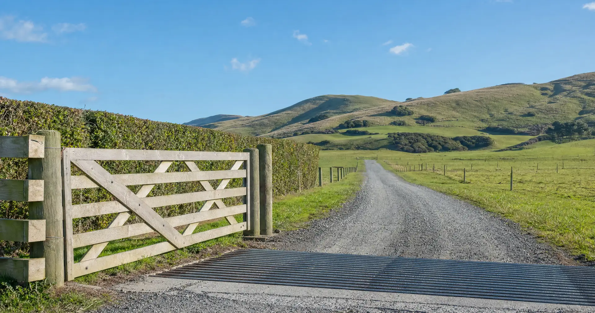 A farm gate on timber posts with a steel cattle stop set into a metalled drive